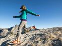 Eine Frau in Trekking-Sandalen läuft einen felsigen Hügel hinunter, mit dem Half Dome in der Ferne.