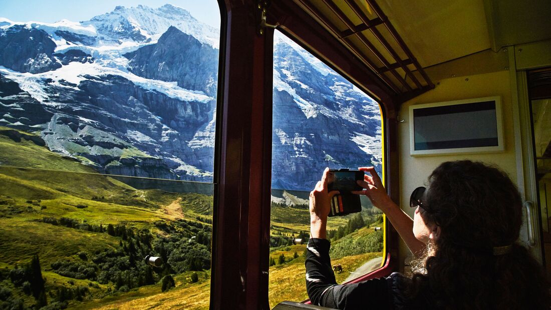 GettyImages/Thomas Barwick: Frau fotografiert Berg mit Smartphone während der Zugfahrt