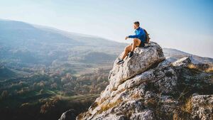 Mann der auf einem Fels sitzt und in die bergige Landschaft blickt
