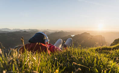 Hiker lying in grass, taking a break and listening music with headphones