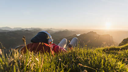 Hiker lying in grass, taking a break and listening music with headphones